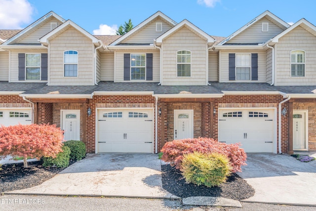townhome / multi-family property with concrete driveway, a shingled roof, brick siding, and an attached garage