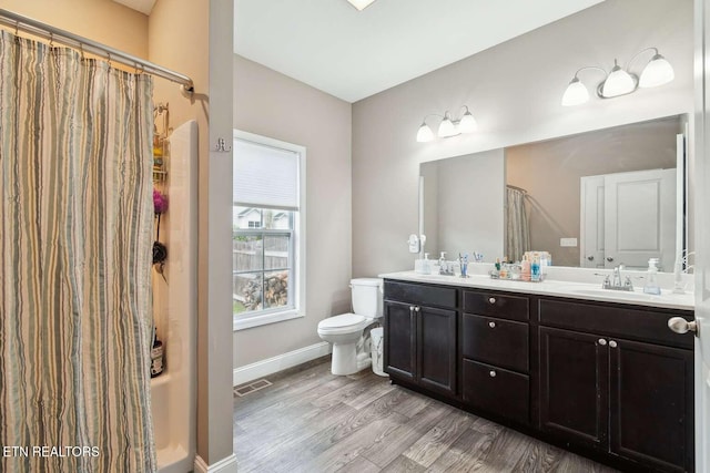 full bath with toilet, wood finished floors, a sink, double vanity, and baseboards