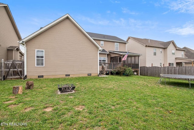 rear view of property featuring a trampoline, a fenced backyard, a sunroom, and crawl space