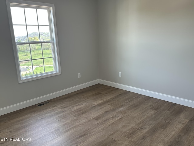 empty room featuring dark wood-style flooring, baseboards, and visible vents