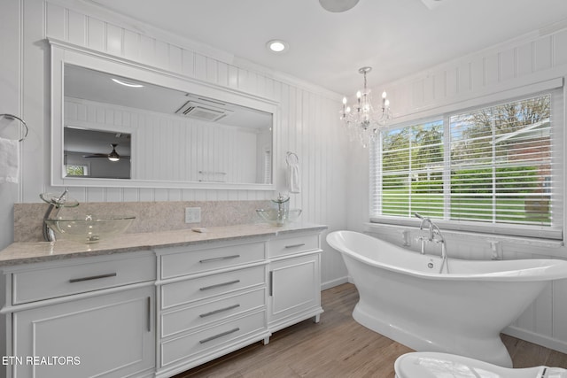 bathroom featuring ceiling fan with notable chandelier, a freestanding tub, vanity, ornamental molding, and wood finished floors