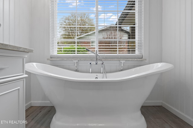full bath with baseboards, a soaking tub, and wood finished floors