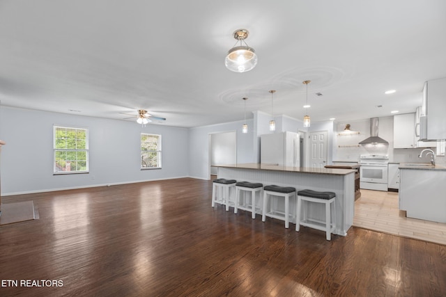 kitchen with a ceiling fan, wood finished floors, wall chimney exhaust hood, and white appliances