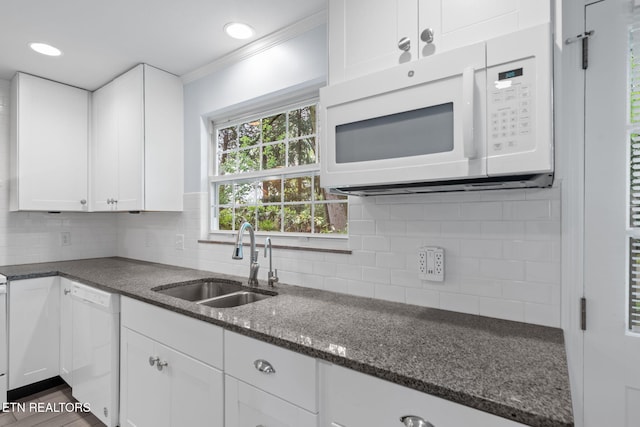kitchen featuring ornamental molding, dark stone countertops, white appliances, white cabinetry, and a sink
