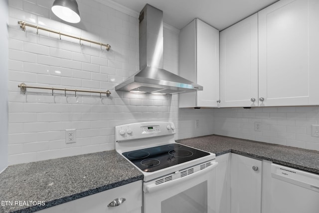 kitchen with wall chimney range hood, white appliances, white cabinetry, dark stone counters, and decorative backsplash