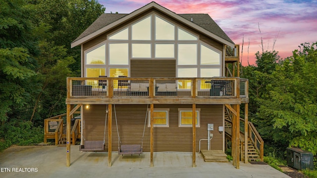 back of house at dusk featuring a patio, a shingled roof, and stairs