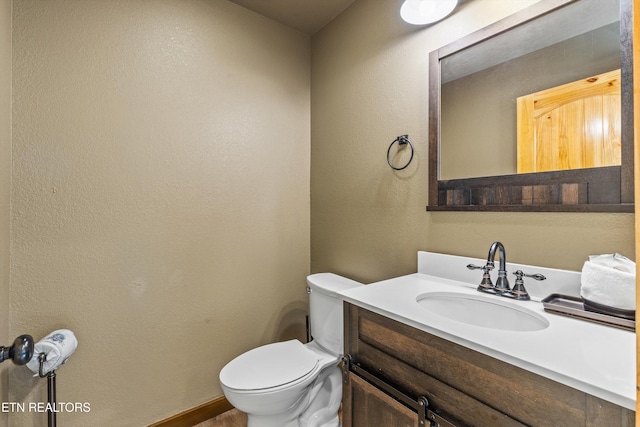 half bathroom featuring toilet, vanity, and a textured wall