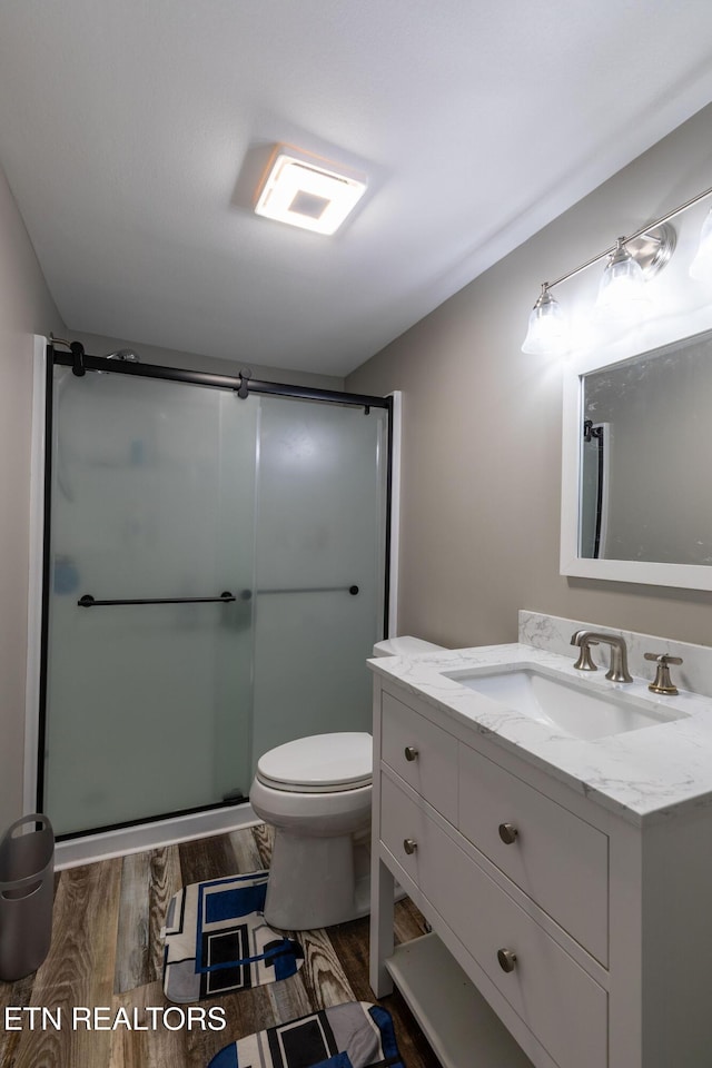 full bathroom with toilet, vanity, a stall shower, and wood finished floors