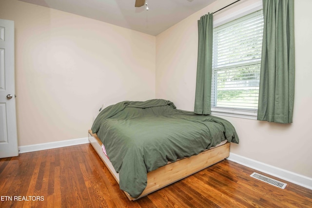 bedroom featuring ceiling fan, visible vents, baseboards, and wood finished floors