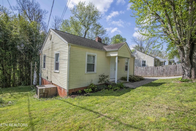 bungalow featuring roof with shingles, a chimney, a front lawn, central AC, and fence