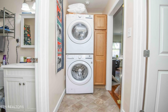 laundry area featuring stacked washer and dryer, cabinet space, and a sink