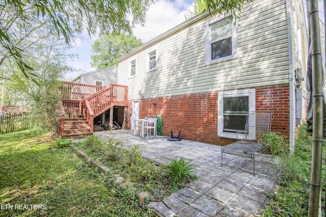 rear view of house featuring a wooden deck, a patio area, brick siding, fence, and stairs
