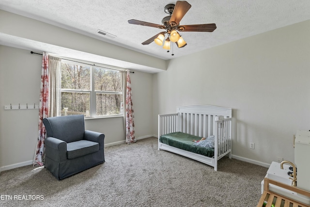 bedroom with a crib, visible vents, carpet, and a textured ceiling