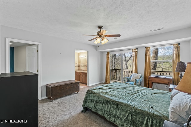 bedroom featuring visible vents, baseboards, a textured ceiling, ensuite bath, and light carpet