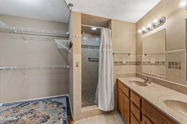full bath featuring a sink, double vanity, tile patterned flooring, a textured ceiling, and a tile shower