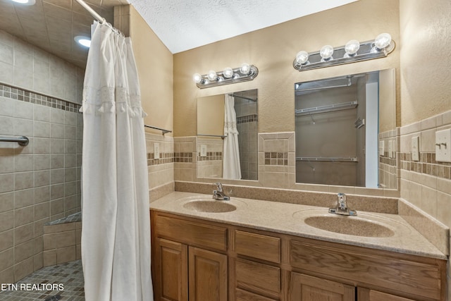 full bath featuring a sink, tile walls, a tile shower, and double vanity