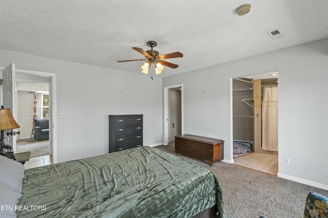 carpeted bedroom with a spacious closet, visible vents, baseboards, and a ceiling fan