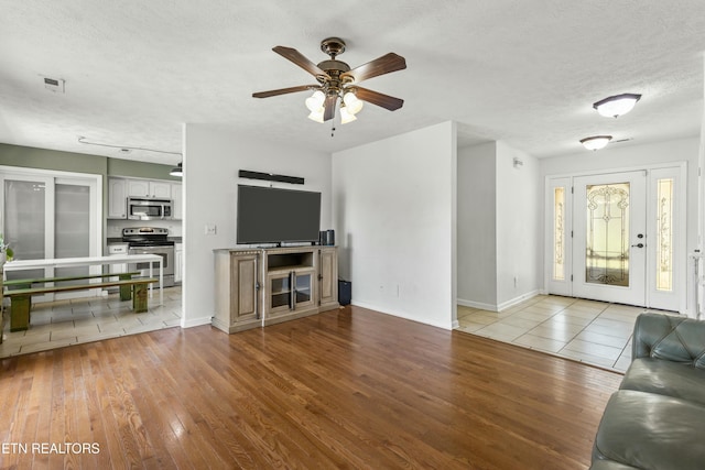 living room with baseboards, a textured ceiling, a ceiling fan, visible vents, and wood finished floors