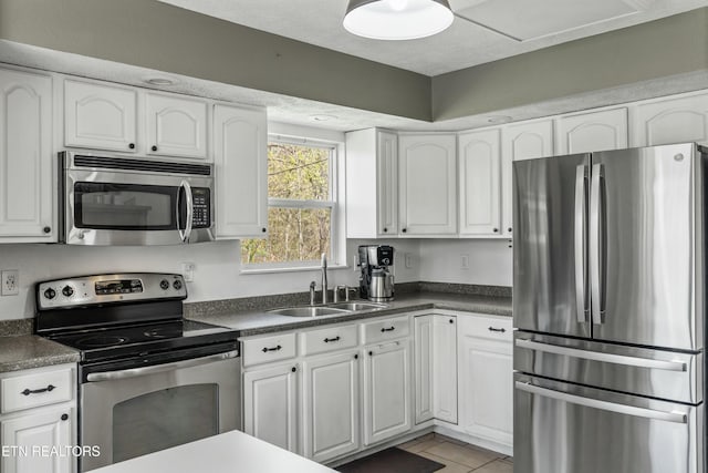 kitchen featuring stainless steel appliances, white cabinets, a sink, and dark countertops