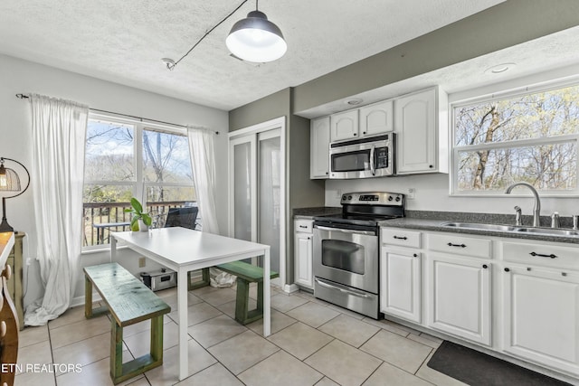 kitchen with a textured ceiling, white cabinetry, dark countertops, a sink, and stainless steel appliances