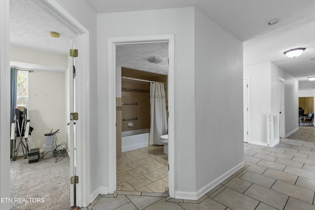 hall featuring a textured ceiling, baseboards, and light tile patterned flooring