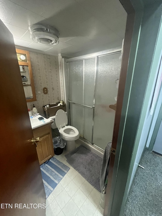bathroom with a shower stall, vanity, tile patterned flooring, toilet, and wallpapered walls