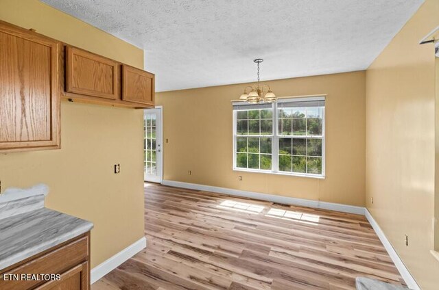 unfurnished dining area with an inviting chandelier, baseboards, light wood-type flooring, and a textured ceiling