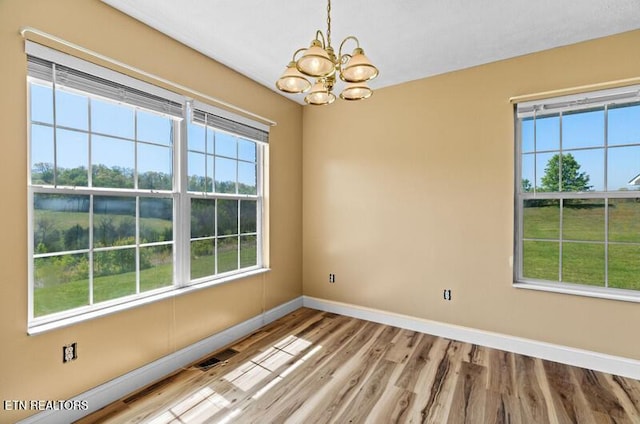 spare room featuring baseboards, wood finished floors, a chandelier, and visible vents