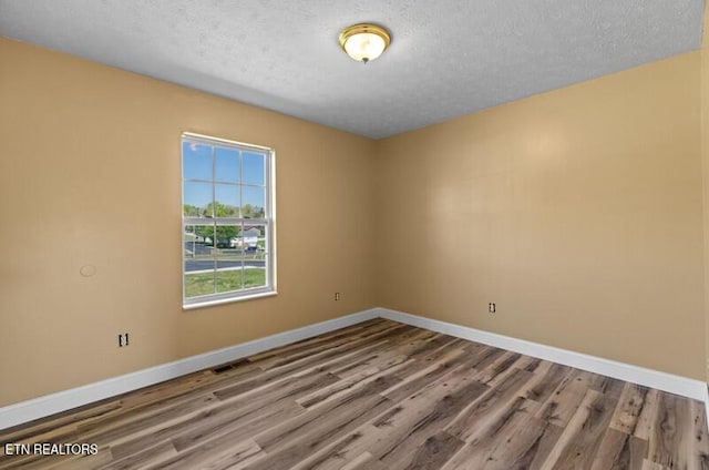 empty room with baseboards, a textured ceiling, wood finished floors, and visible vents