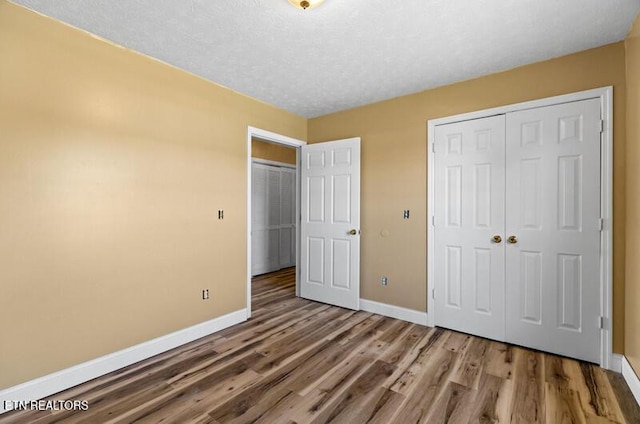unfurnished bedroom with a textured ceiling, baseboards, a closet, and wood finished floors