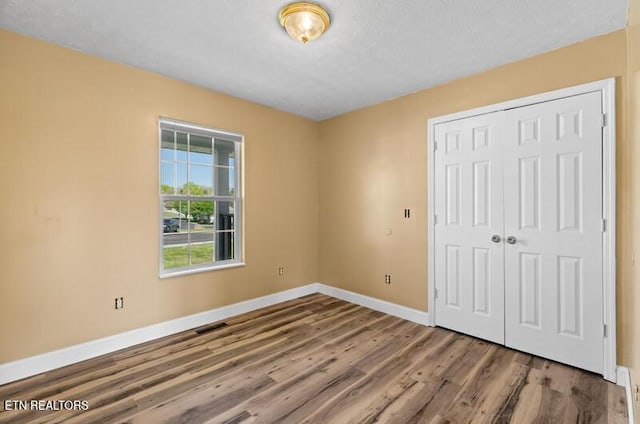 unfurnished bedroom with baseboards, a closet, wood finished floors, and visible vents