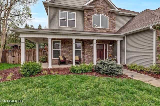 view of front of home with stone siding, fence, a front lawn, and covered porch