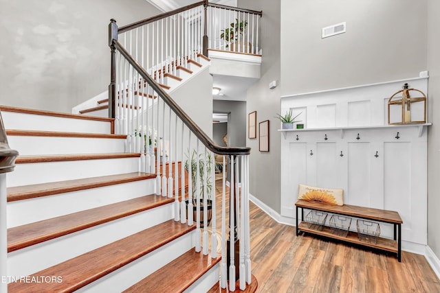 staircase with baseboards, wood finished floors, a high ceiling, and visible vents