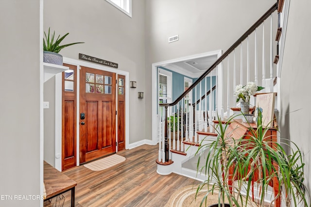 entrance foyer featuring visible vents, baseboards, stairway, a towering ceiling, and wood finished floors