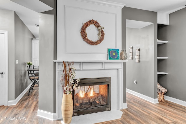 room details with built in shelves, baseboards, a warm lit fireplace, and wood finished floors