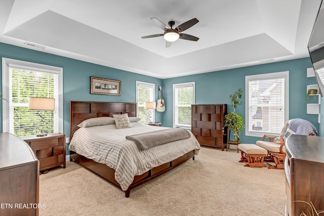 bedroom featuring visible vents, a raised ceiling, light colored carpet, and a ceiling fan