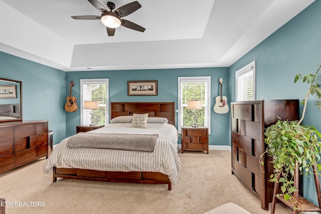 bedroom featuring light carpet, ceiling fan, baseboards, and a raised ceiling