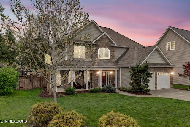 traditional-style home with driveway, stone siding, fence, and a lawn