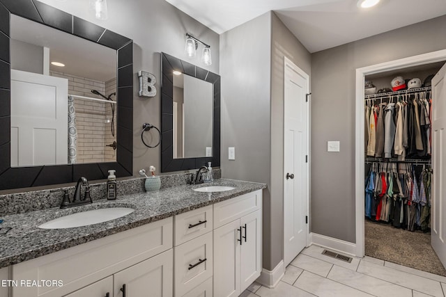 bathroom featuring tiled shower, double vanity, visible vents, and a sink