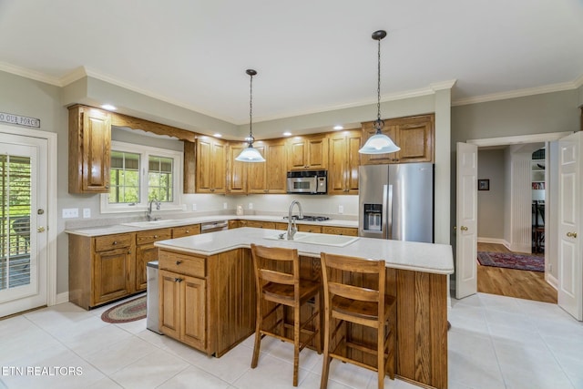 kitchen with ornamental molding, light countertops, appliances with stainless steel finishes, brown cabinetry, and a center island with sink
