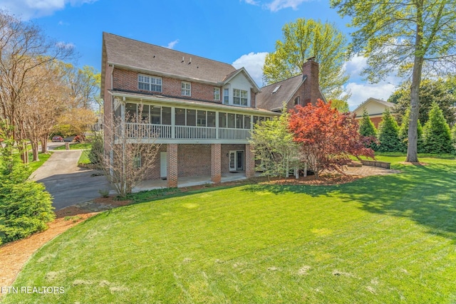 rear view of house featuring a patio, brick siding, a sunroom, and a lawn