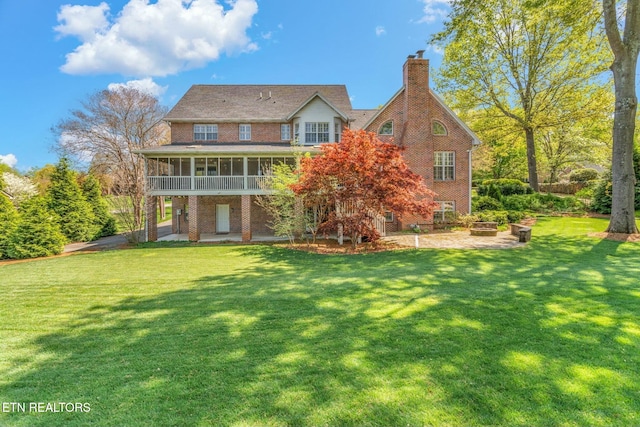 rear view of house with a sunroom, a lawn, a patio area, a fire pit, and brick siding