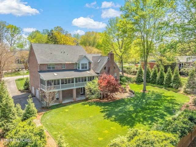 back of property with a garage, aphalt driveway, a chimney, and a lawn