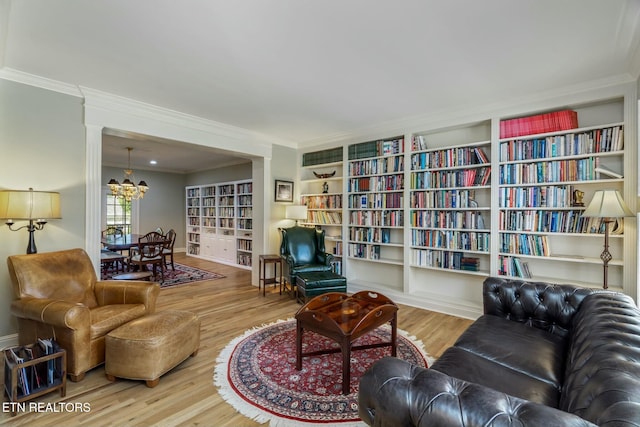 living area featuring bookshelves, an inviting chandelier, crown molding, and wood finished floors