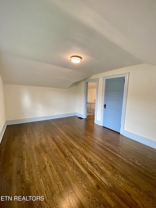additional living space featuring baseboards, dark wood-style floors, and lofted ceiling