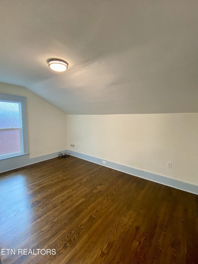 bonus room with dark wood-style flooring, baseboards, and vaulted ceiling