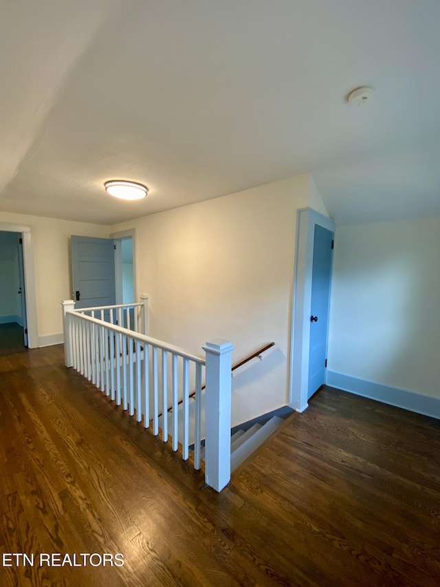 hallway with an upstairs landing, baseboards, and dark wood finished floors