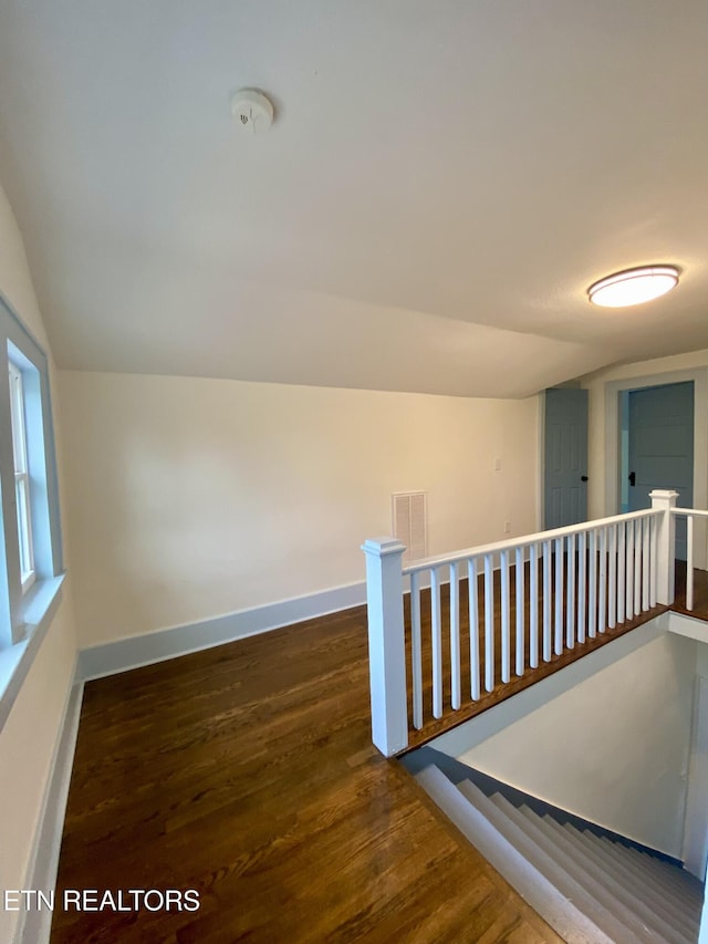 hallway with an upstairs landing, baseboards, lofted ceiling, and wood finished floors