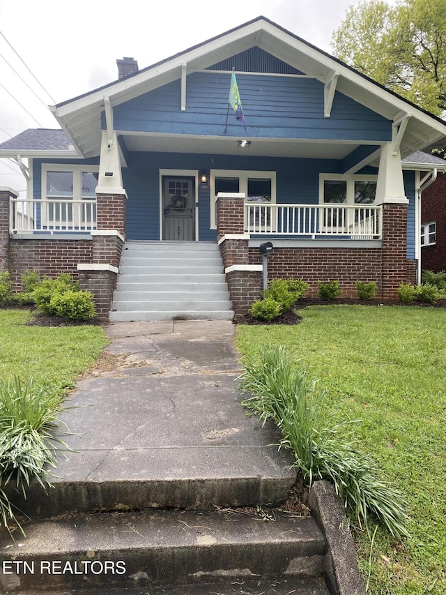 view of front of house featuring a chimney, covered porch, and a front lawn