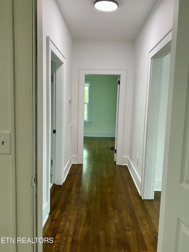 hallway featuring dark wood-type flooring, visible vents, and baseboards